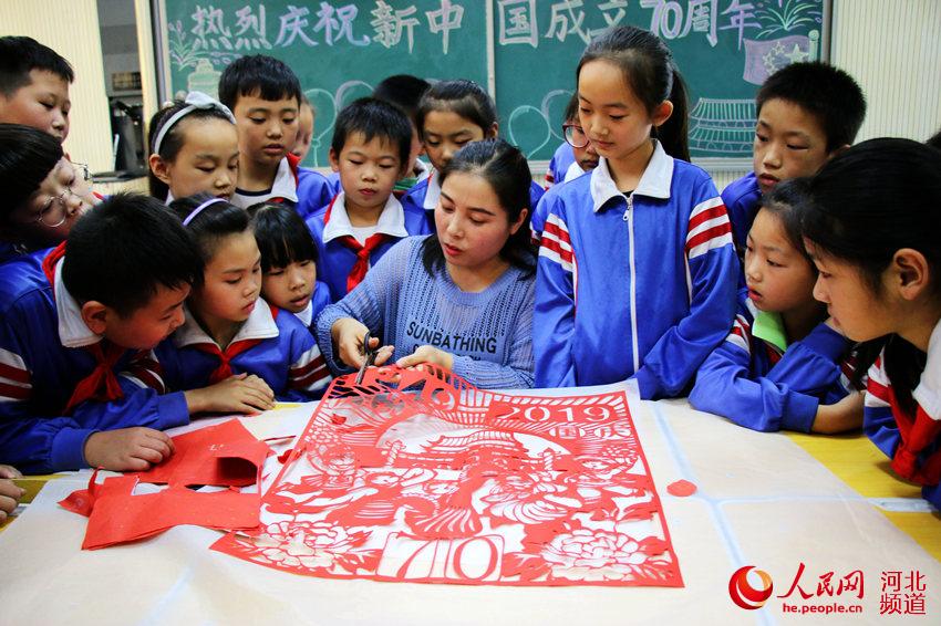 图为广平县广平小学学生在剪纸艺术课上跟着老师创作国庆剪纸作品。