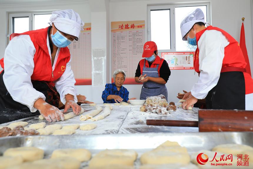 唐山市滦南县西胡各庄村养老小食堂里志愿者和老人围坐在一起亲手制作月饼。张永新摄