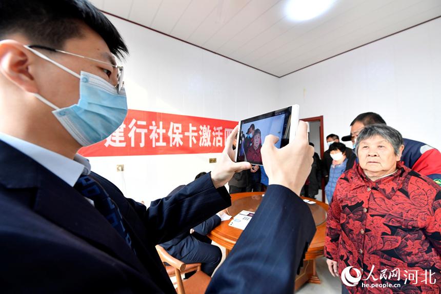 2021年12月15日,在河北省文安县小务农场小务村村委会,银行工作人员为村民办理社保卡激活手续。 王晖摄