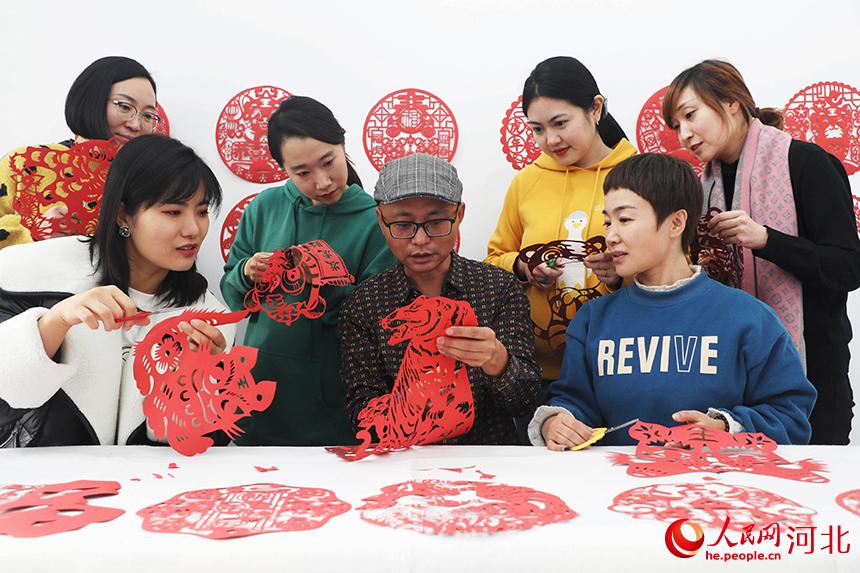 在河北省唐山市丰润区太平路街道同安社区，剪纸艺人在教居民创作虎主题剪纸作品。 朱大勇摄