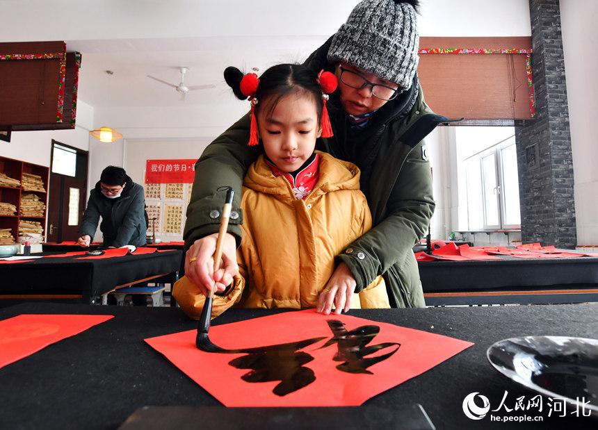 1月25日，在河北省迁安市扣庄镇新时代文明实践所，书法爱好者指导孩子写“福”字。 梁玉水摄