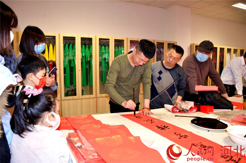 现场群众围在桌旁,欣赏对联的创作过程。 定兴县委宣传部供图