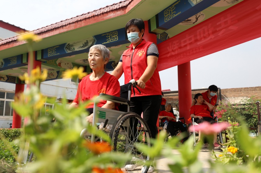 隆尧县魏庄镇中心卫生院医养结合健康中心，志愿者推着老人在小公园赏景。 成梅摄