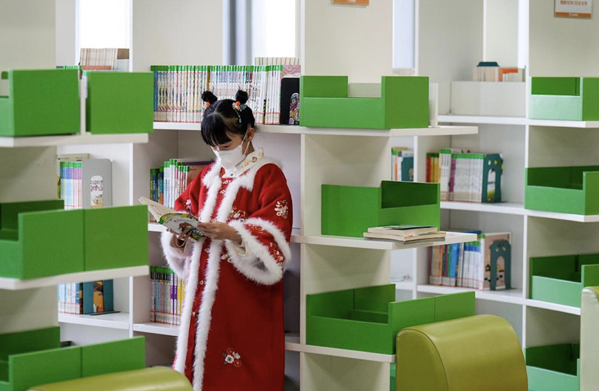 春节假期，图书馆内一位身着汉服的小姑娘在书架旁阅读喜欢的图书。 赵亮摄