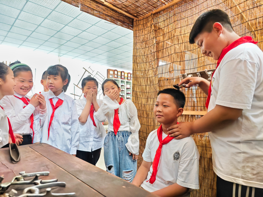 在唐坊民俗博物馆，唐坊中心小学学生在体验用老式理发工具理发。 张杰摄