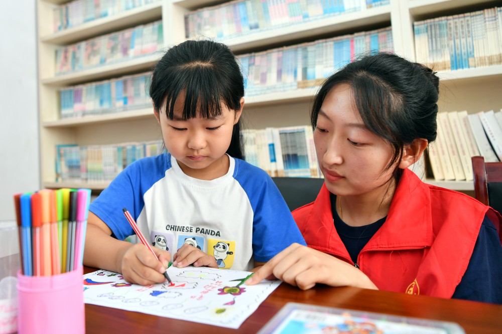 8月10日,在迁安市沙河驿镇唐庄子村农家书屋内,大学生志愿者唐琳茹陪儿童绘制“家庭文明“主题画。 彭月娟摄