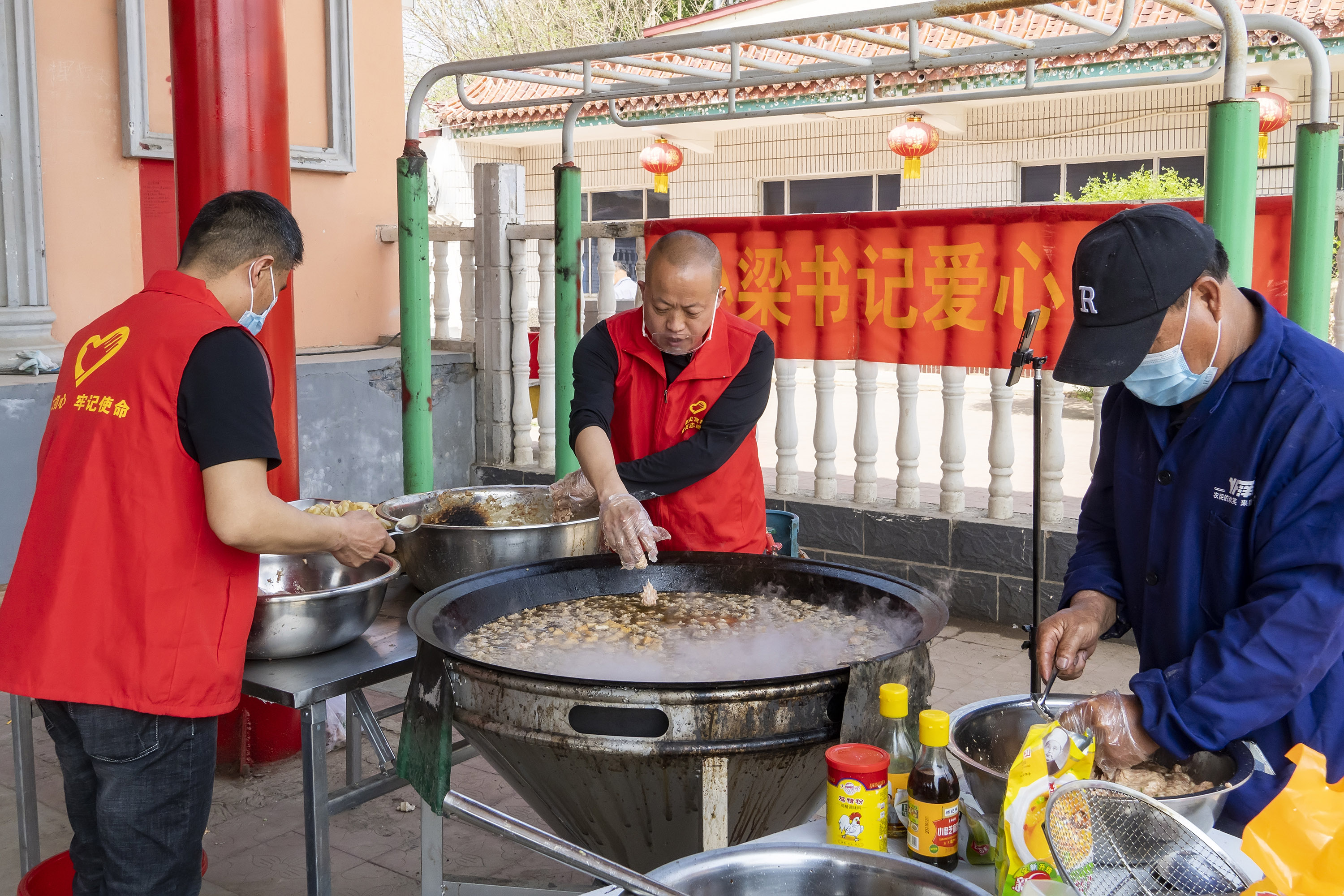 4月17日，高阳县南尖村爱心午餐制作现场，小梁书记（中）带领志愿者在熬菜中放入肉丸子。芦建勇摄
