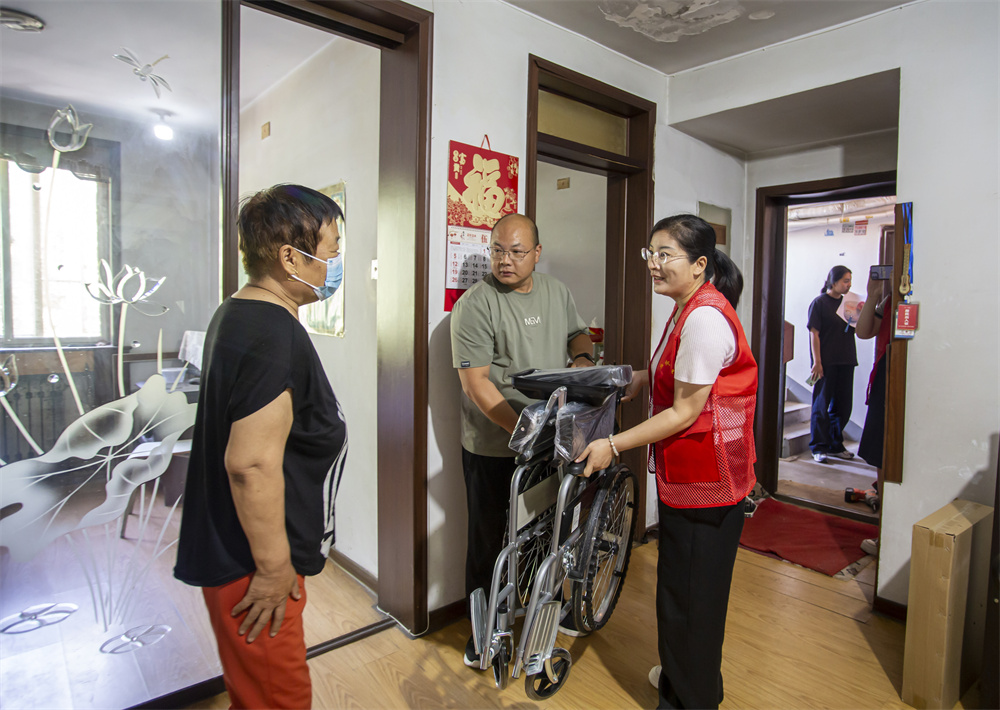 在河北省邯鄲市復興區鐵路大院街道九一社區，區民政局工作人員和社區志願者為困難半失能老人高四景贈送輪椅。聶長青攝