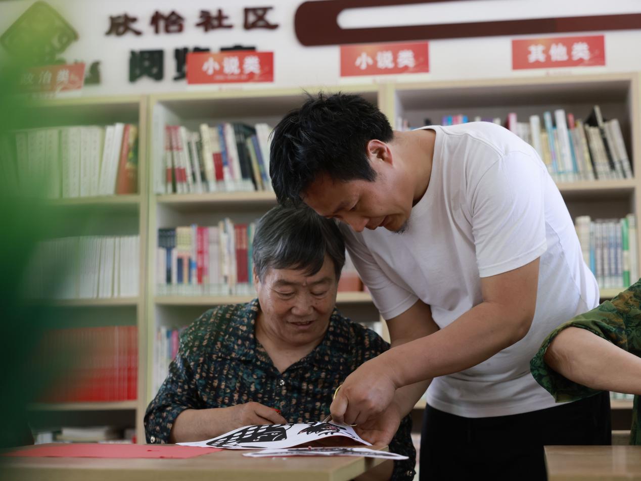 剪纸技艺传承人石飞（右）为居民讲解剪纸技巧。杨晨摄