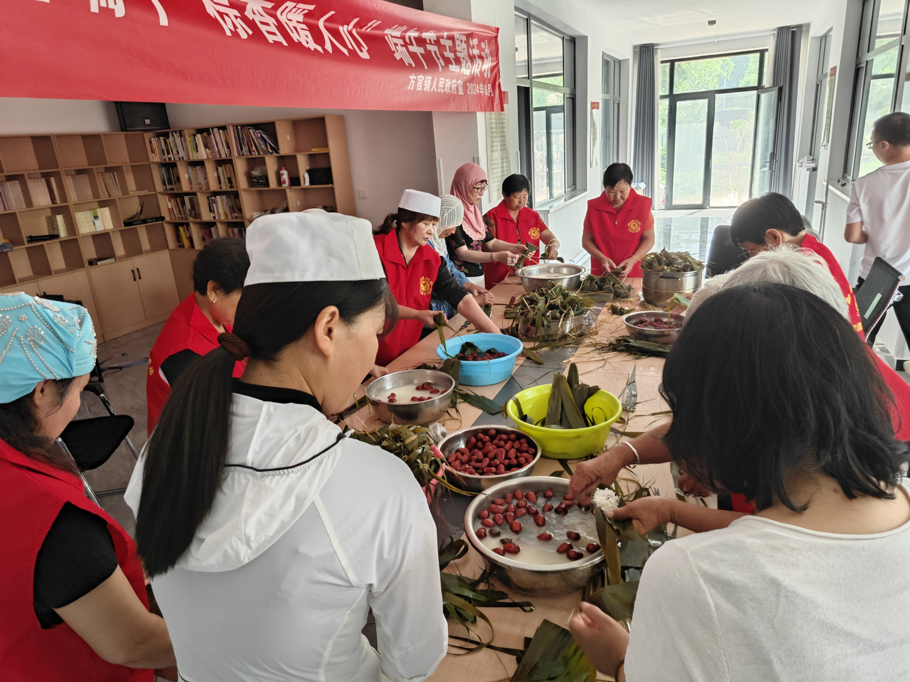 6月6日，在高碑店市方官镇方官村互助幸福院，志愿者与村民围在一起包粽子。薛鲁源摄
