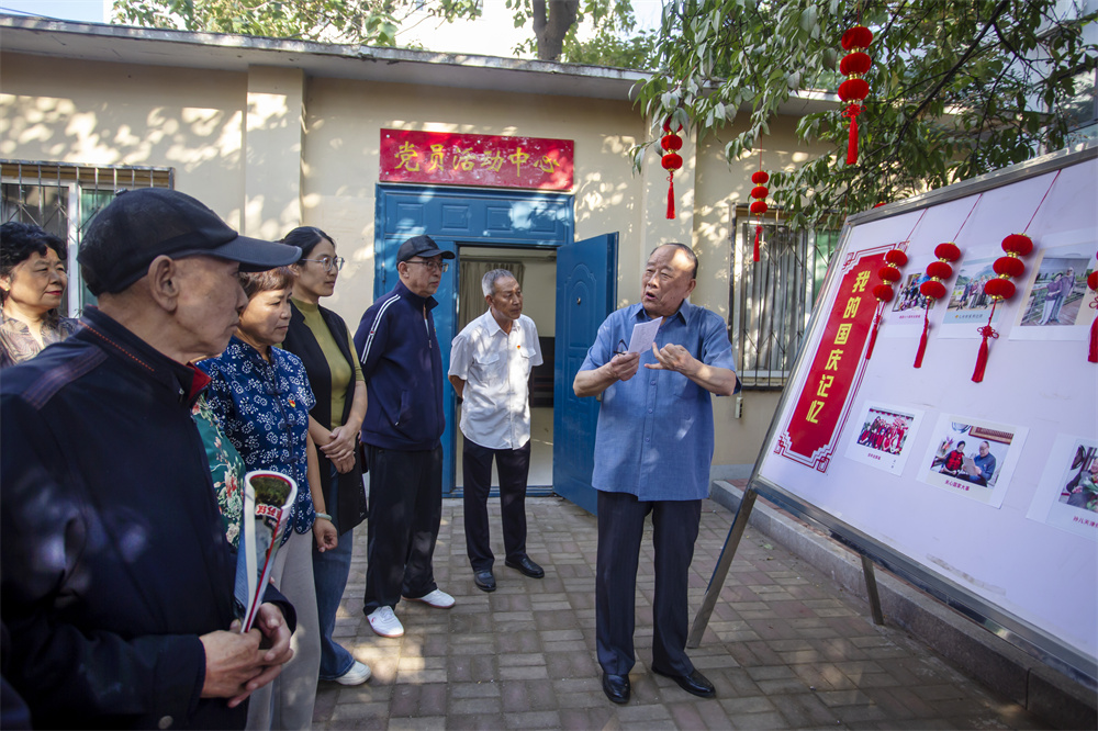 9月24日，河北省邯郸市复兴区化林路街道建西一社区，退休干部赵鸿皎正在为居民讲述其拍摄的家庭相册和社区各方面的变化照片，见证伟大祖国发生的巨大变化。聂长青摄