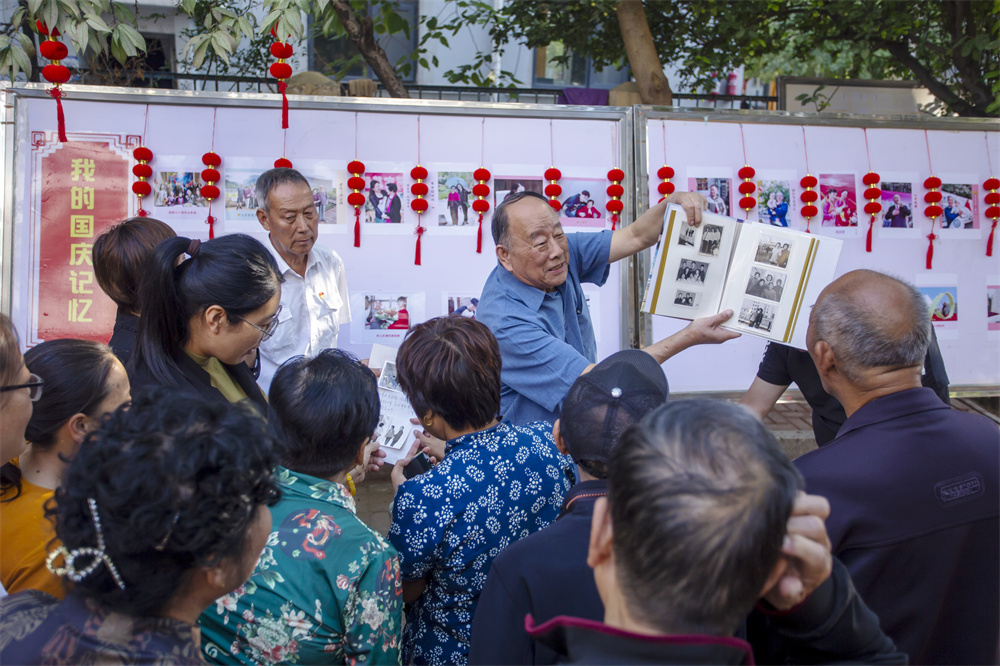 9月24日,河北省邯郸市复兴区化林路街道建西一社区,退休干部赵鸿皎正在为居民讲述其拍摄的家庭相册和社区各方面的变化照片,见证伟大祖国发生的巨大变化。聂长青摄