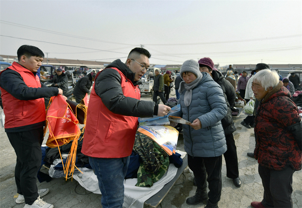 志愿者向摊主发放宣传手册，讲解气象科普知识。梁玉水摄