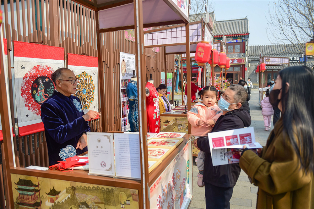 河间剪纸艺人（左一）在“三八”非遗市集向市民介绍其作品。傅新春摄