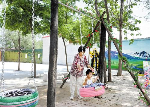 5月17日，在威縣馬家庄村廣場上，一位村民帶著孫子在廢輪胎制作的秋千上玩耍。 本報記者 呂若汐攝