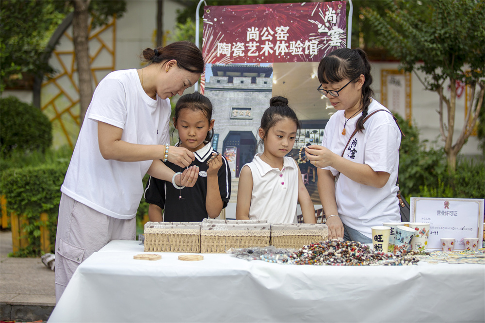 2025年7月4日，河北省邯鄲市復興區百花小學第二屆“花朵集市”在操場熱鬧開市，民間手工藝人在教同學們做陶瓷手鏈。聶長青攝