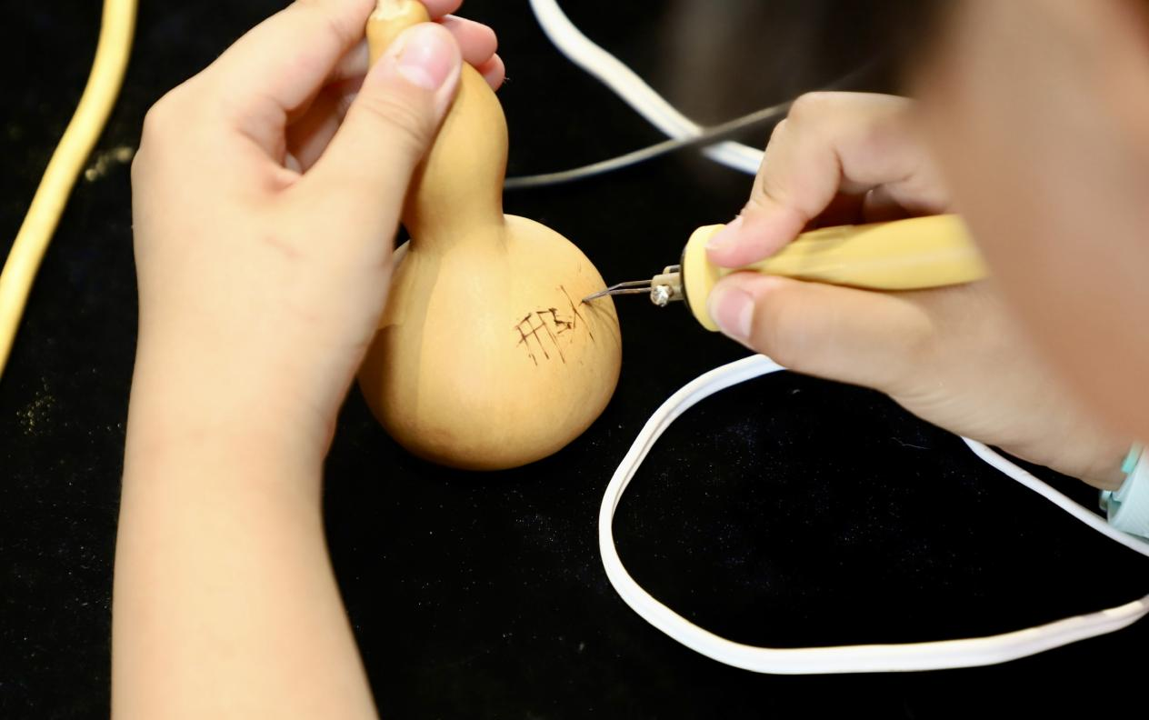 一名孩子在葫芦上烙上自己的姓名。陈雷摄