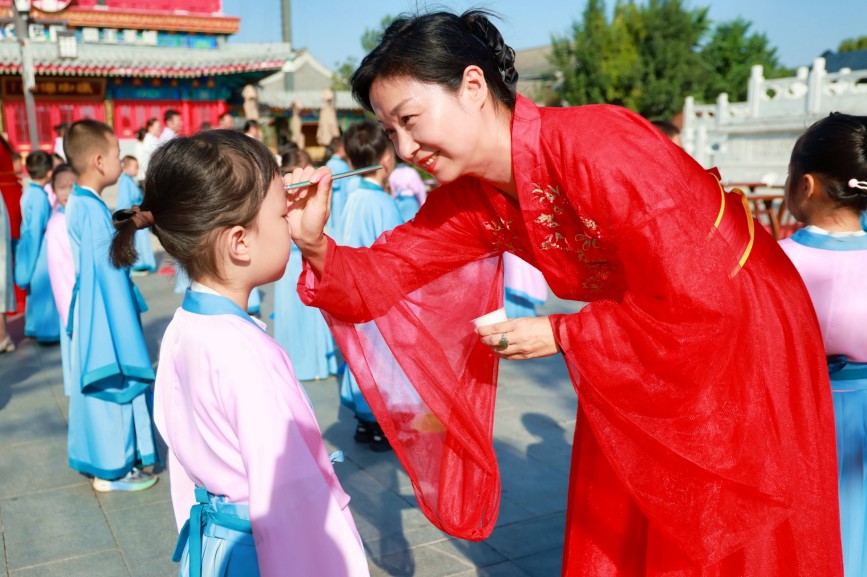 老师用毛笔蘸朱砂在孩子额头点红痣,寄托美好祝愿。杨洋摄