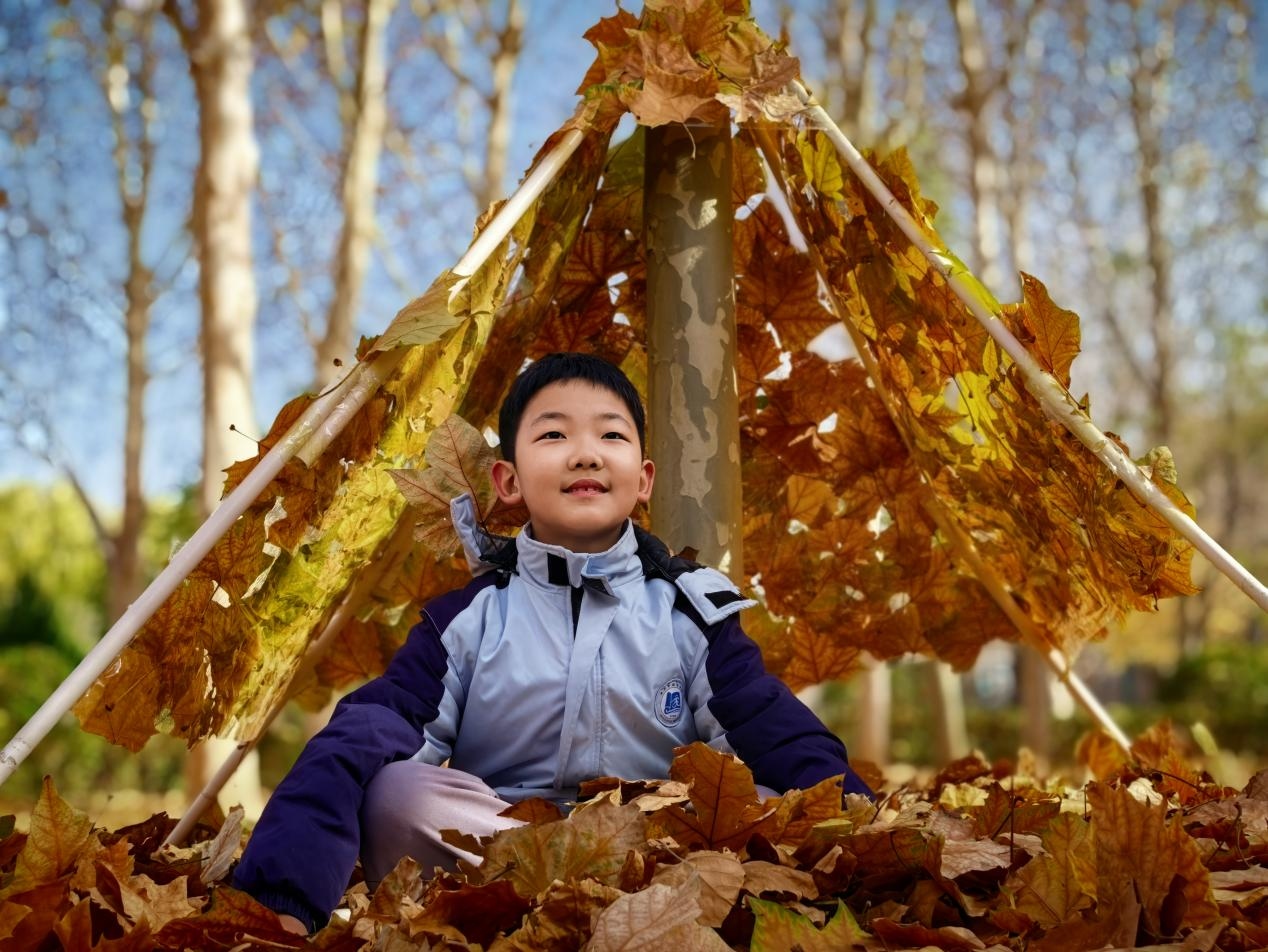学生坐在和伙伴们共同搭建的落叶帐篷里。张玉华摄