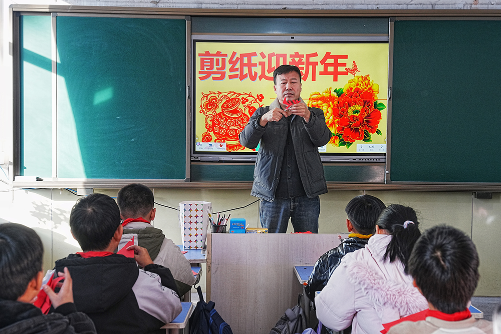 12月25日,非物质文化遗产代表性传承人走进沙河驿镇北铺完全小学教学生们剪纸。张泽慧摄