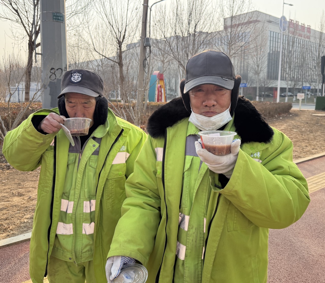环卫工人喝着热气腾腾的腊八粥，满面笑容。吴胜园摄