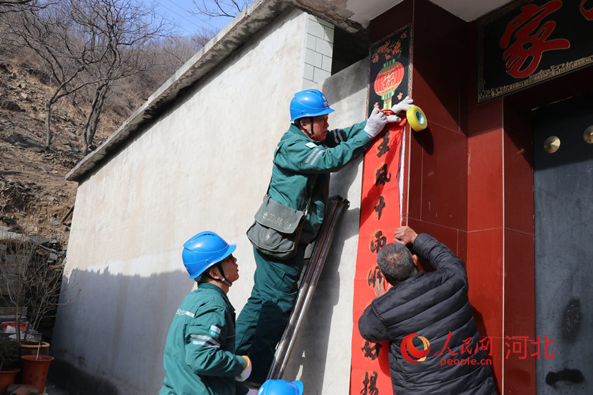 国网赞皇供电公司嶂石岩服务站贾立杰和同事在帮村民贴春联。人民网记者 祝龙超摄