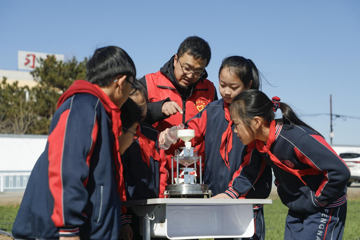 丰南区气象局的工作人员为四神庄小学的学生演示翻斗式雨量计。陈军摄