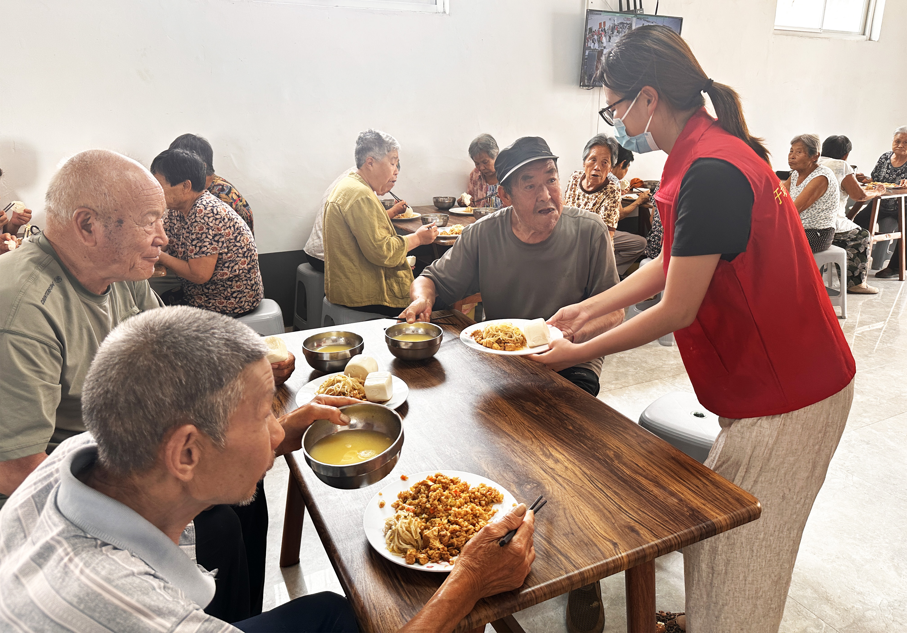 8月5日中午，在於堤村老年食堂，志願者幫行動不便的老人打飯。石艷宣攝